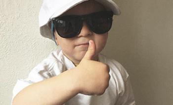 Un niño con una gorra demasiado grande y lentes de sol con el pulgar hacia arriba